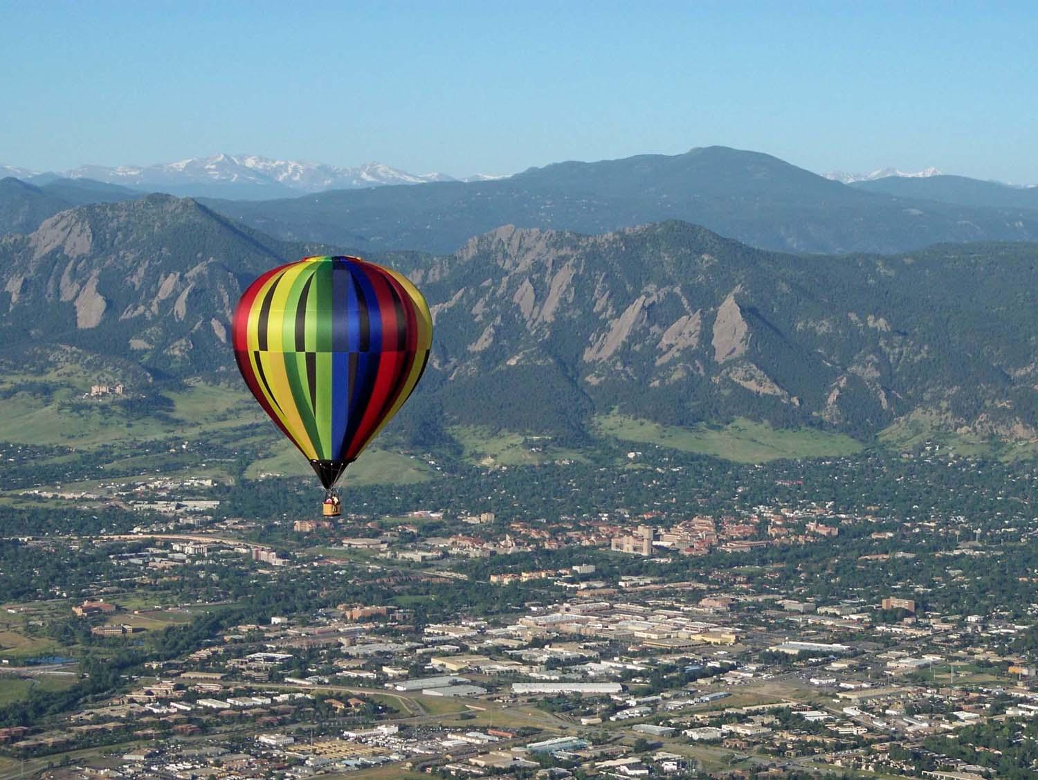 A rainbow-colored balloon hovers over the cityscape of Boulder, with its famous Flatiron mountains off in the distance