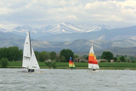 A sailboat with white sails and one with an orange and red one cruises across choppy waters