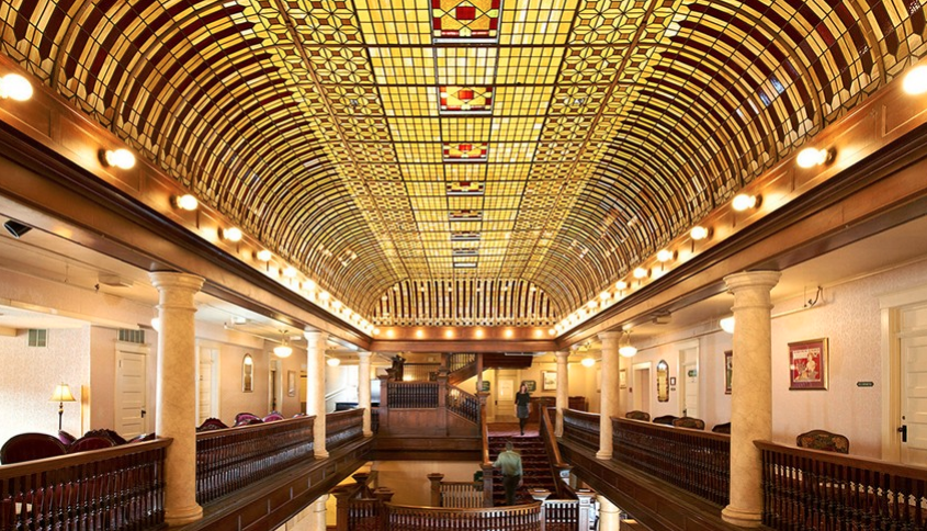 An intricately designed stained-glass ceiling seems to glow above the line of exposed-bulb lighting at the Hotel Boulderado in Boulder, Colorado.