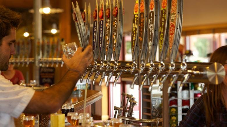 A row of wooden taps, each with the logo of its beer, is pulled by the bartender