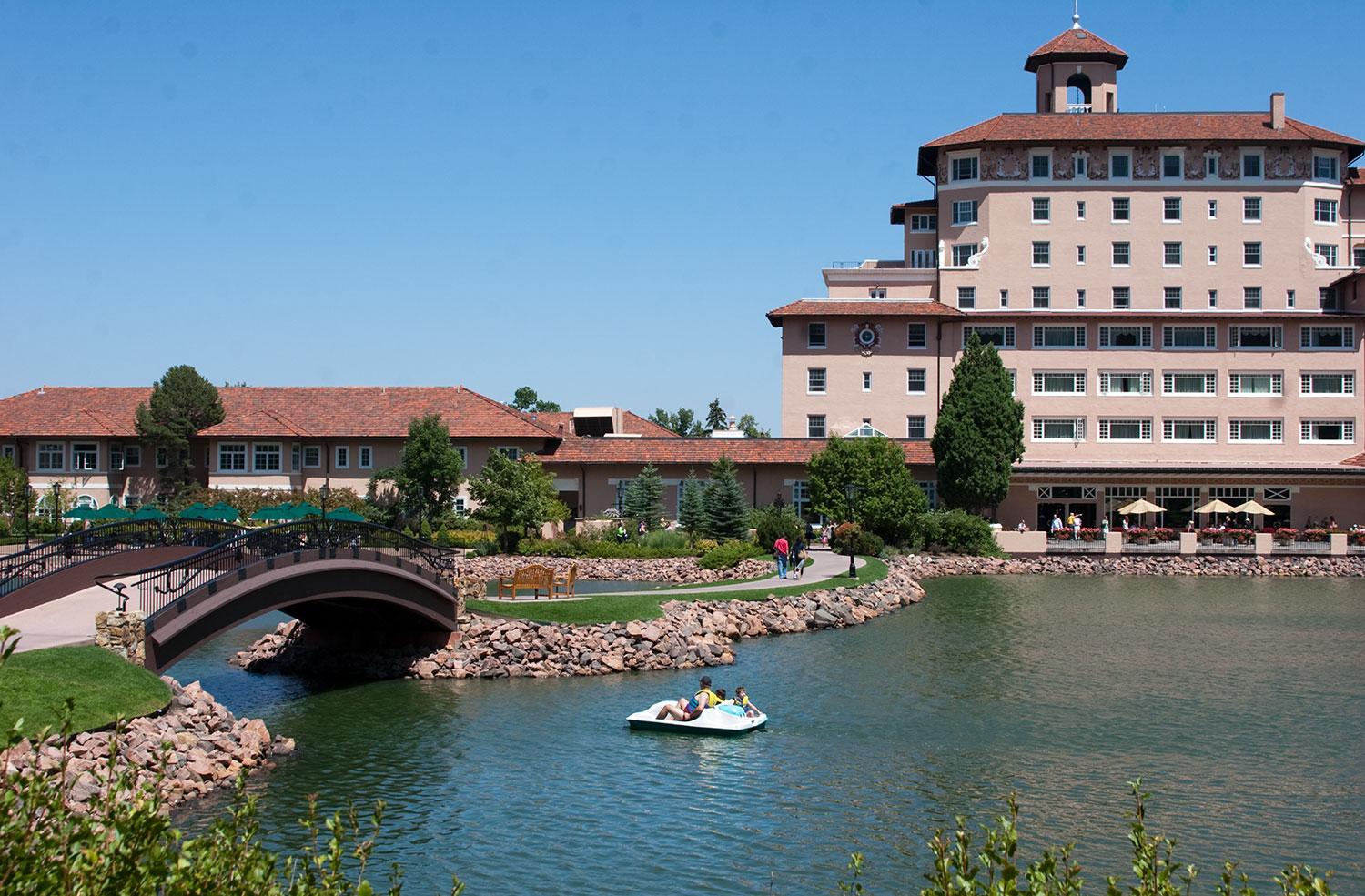 People peddle in a white paddle boat towards a small pedestrian bridge that goes over the body of water outside the Broadmoor hotel in Colorado Springs.