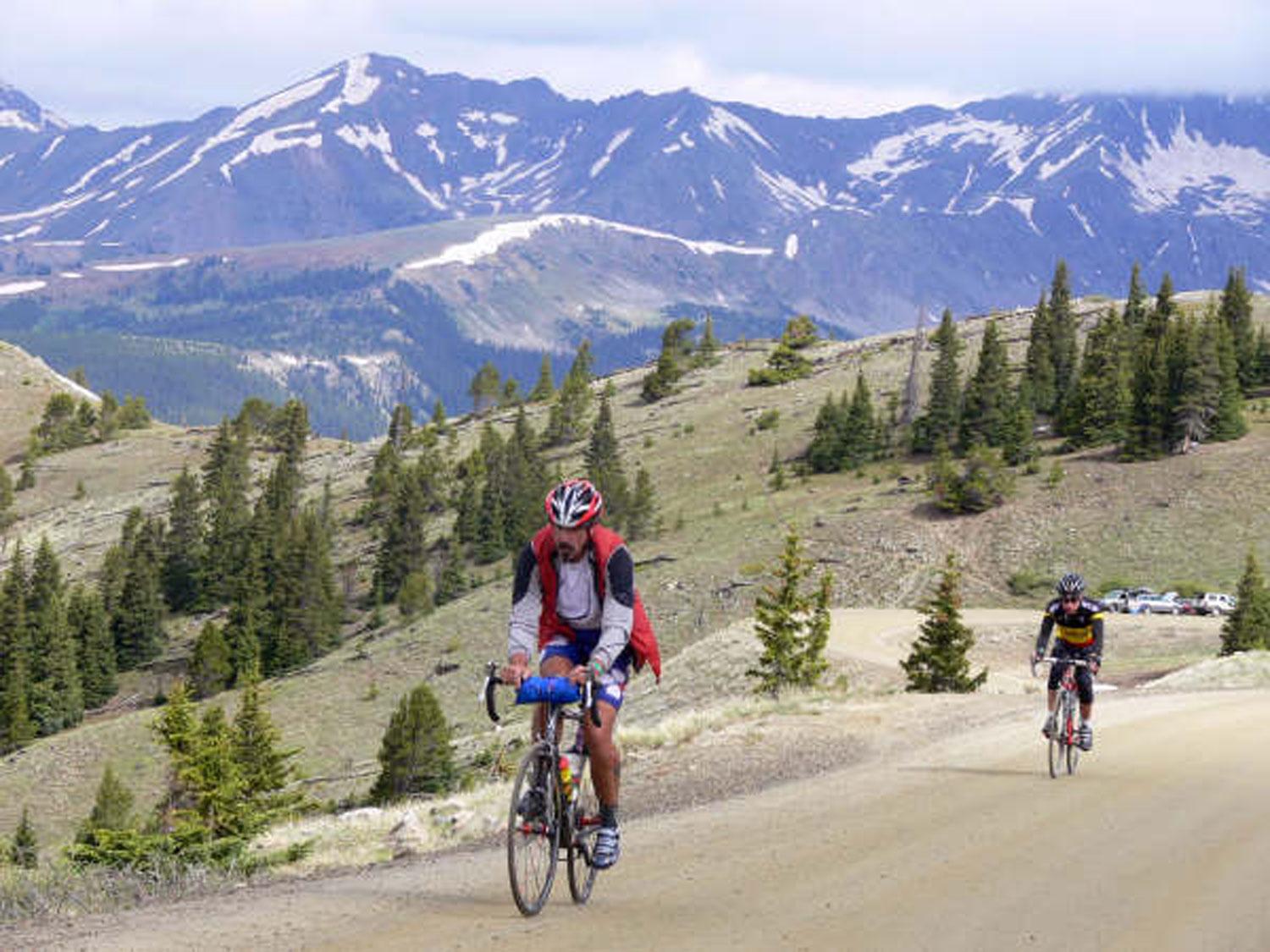 A bicyclist rides along a scenic road with mountains in the background