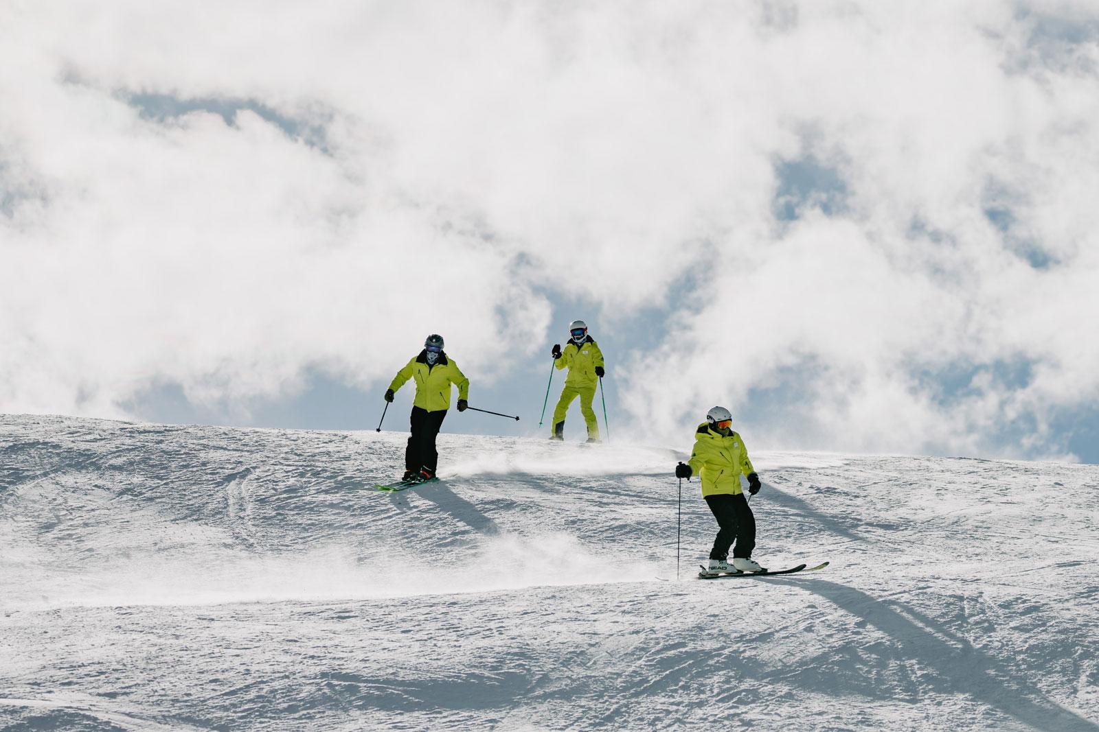 Three skiers in matching neon-yellow jackets ski over small bumps near Aspen, Colorado.