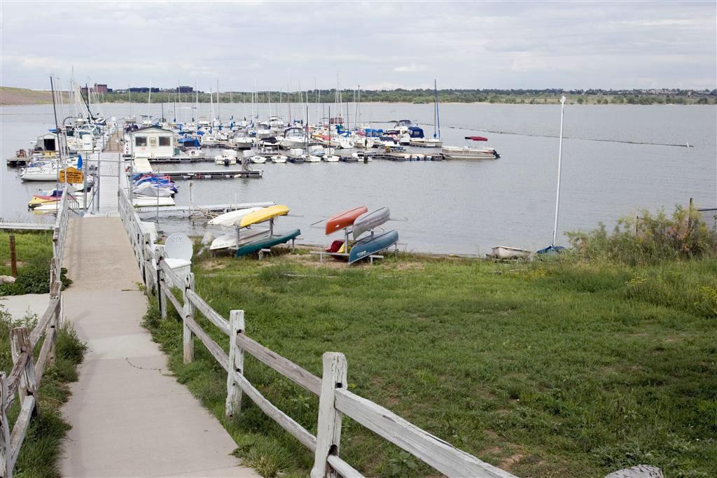 Dozens of sailboats, motorboats and canoes line a pier. A trail to the pier is lined by a white fence.