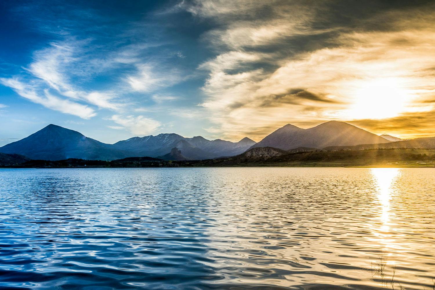 The sun is setting over the Blue Mesa Reservoir with half the image bathed in the golden light of the sun and the other in a blue-hue. 