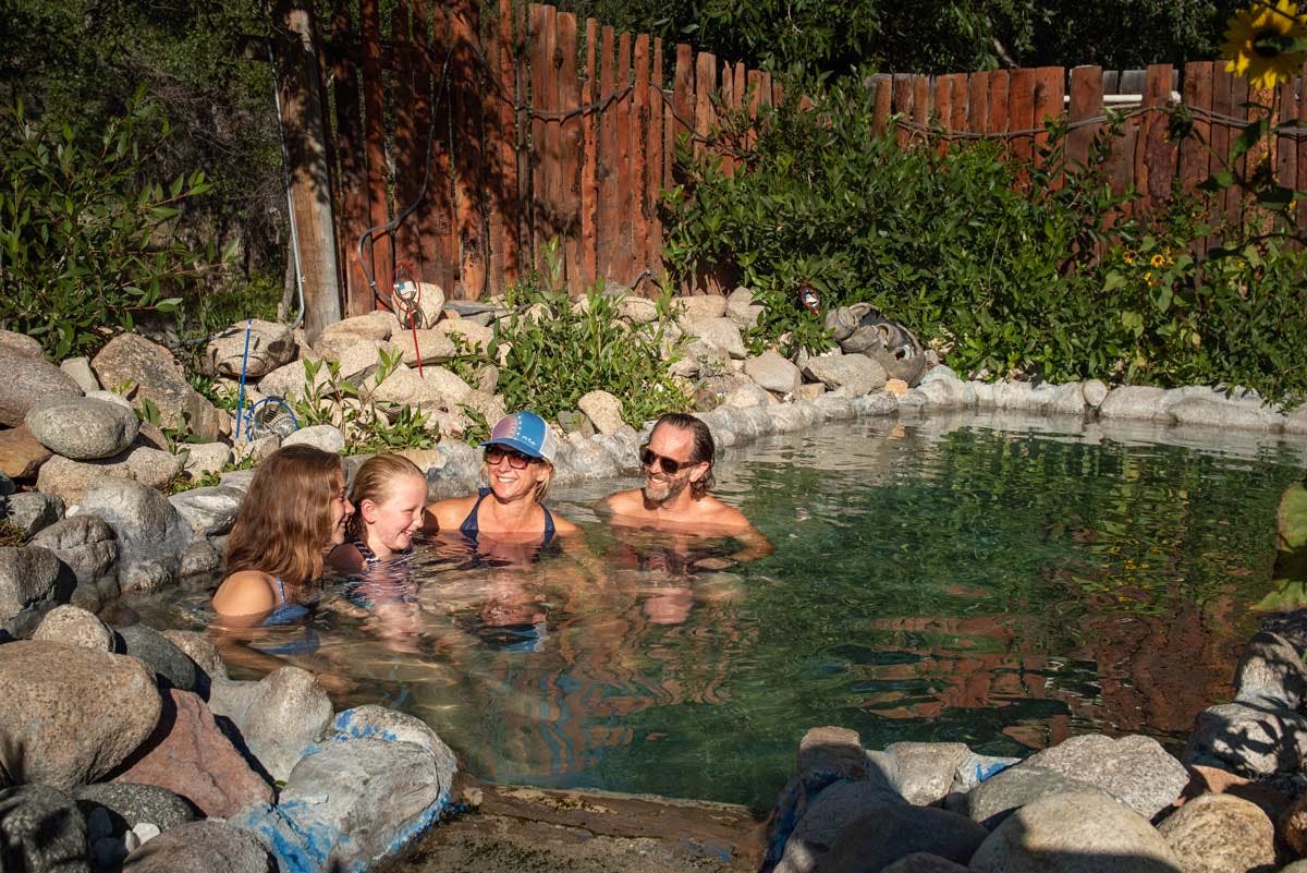 A family sits in a rocky pool at Cottonwood Hot Springs Inn & Spa in the summer with greenery surrounding them.