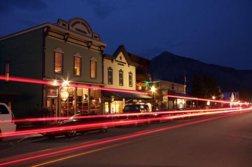 Historic structures on Crested Butte's main drag are lit up at night. The sky is a deep midnight color and traffic lights are bright.