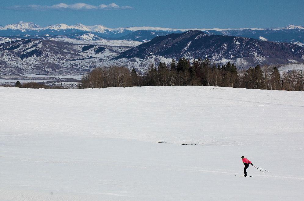 In a vast, flat, snowy meadow, a cross-country skier in a red jacket pushes foward using their poles