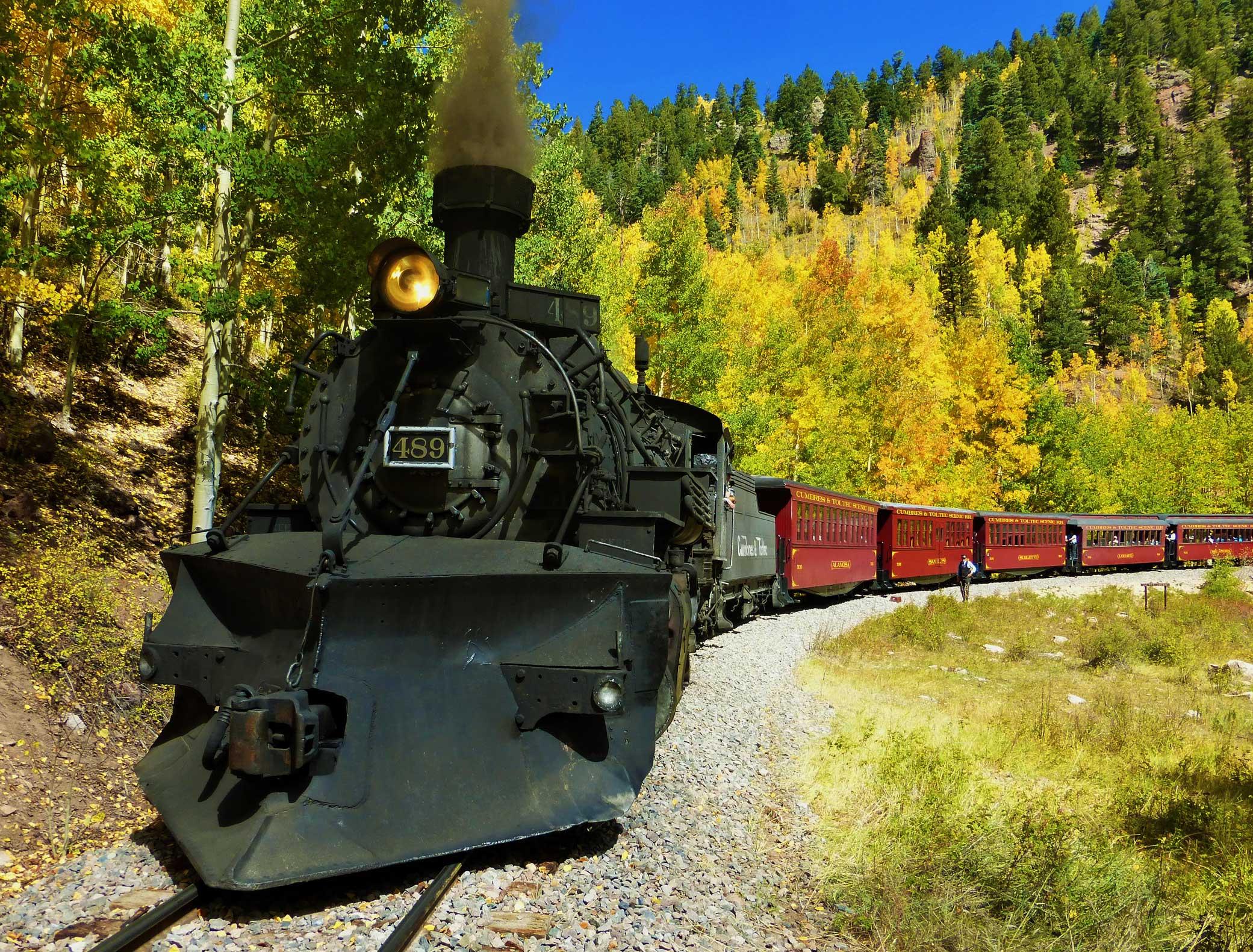 A black train engine with the number 489 on the front pulls crimson, enclosed passenger cars along a track in Colorado.