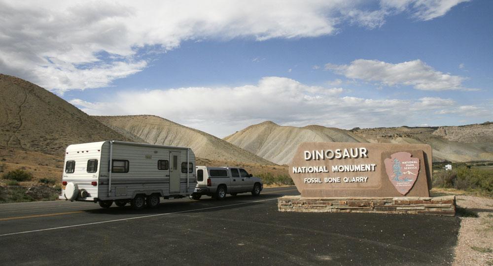 A white truck pulls an RV on the road at the entrance to the monument