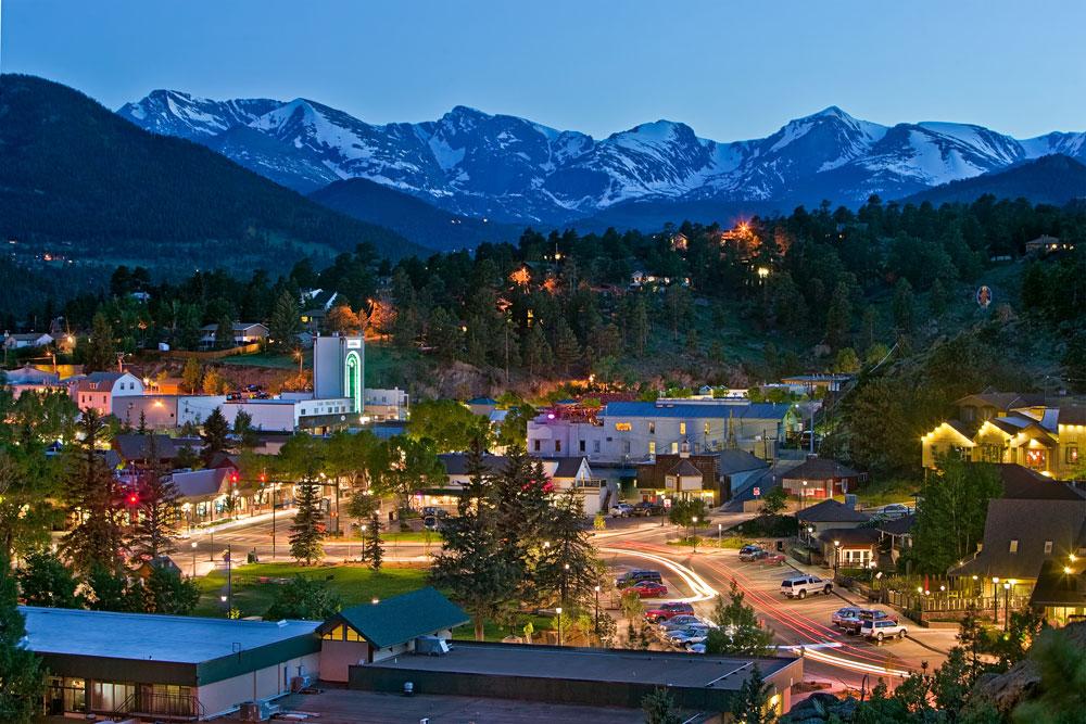 The snowy, white mountain appear to be aglow above the bustling, lit up town of Estes Park, Colorado. 