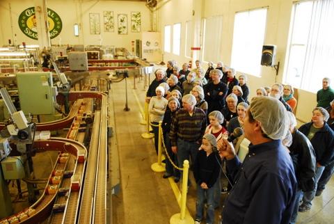 A tour group, all wearing hairnets, look at the boxing machinery at a tea factory