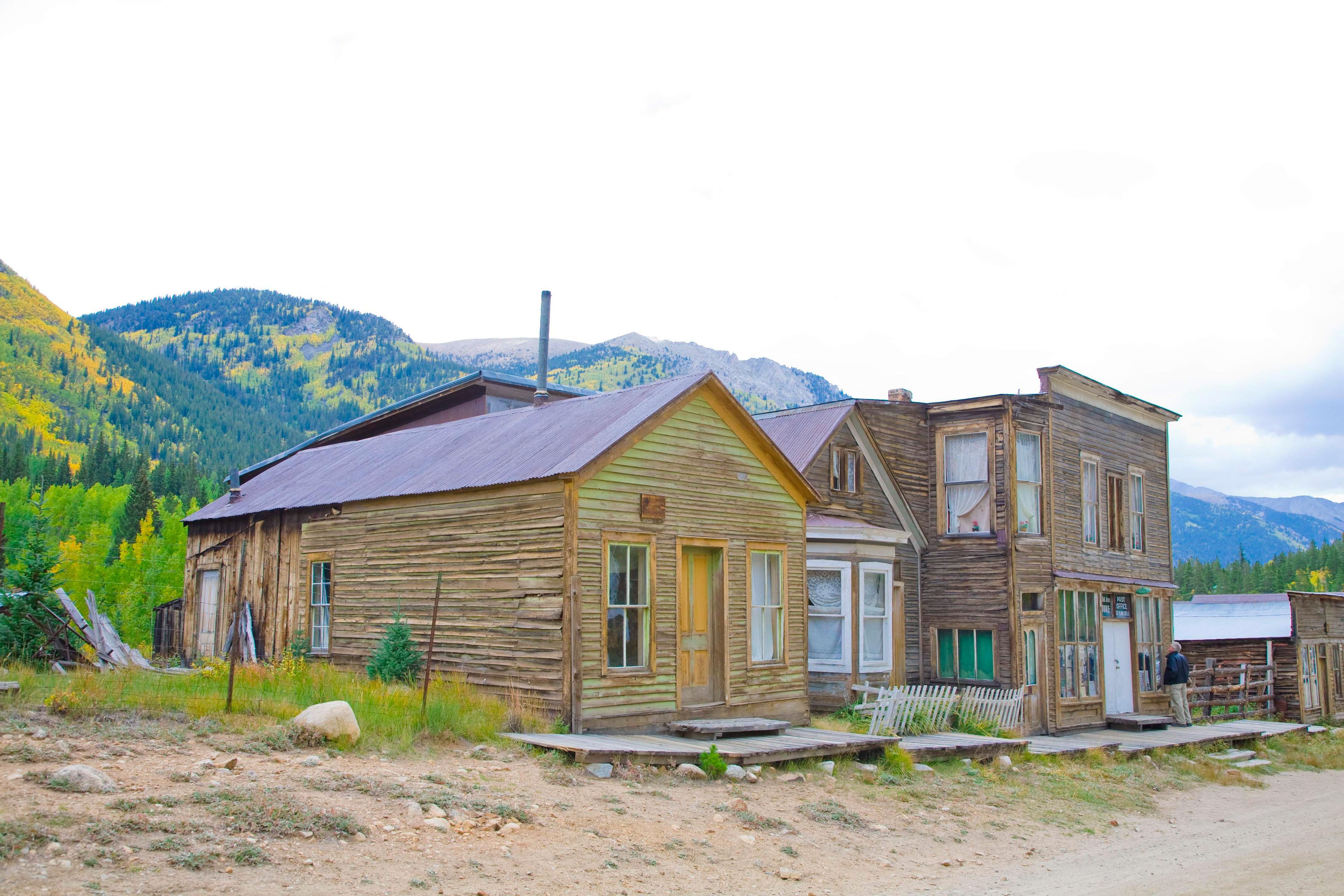 The wooden houses and town buildings of St. Elmo ghost town sit underneath mountains covered in evergreen and golden aspen trees.