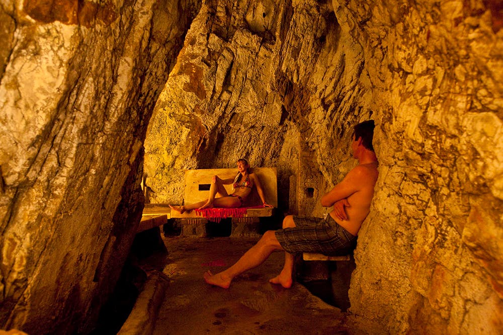 A woman and a man sit in a yellow-hued rock-walled cave at Yampah Spa. 