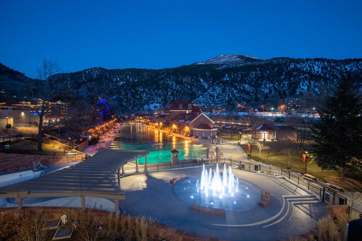 The snow atop the mountains outside Glenwood Hot Springs Resort glows under the moonlight. The resort waters a lit blue and green by lights.