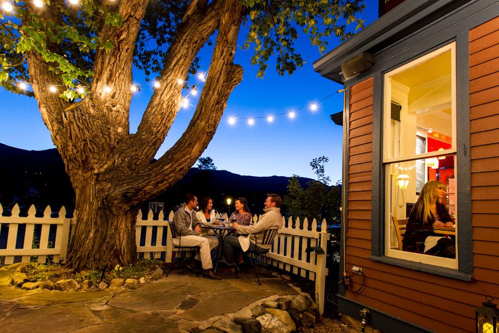 The dark evening sky is settling in and a string of lights wrapped around an old tree illuminate four people eating dinner around an outdoor table in Breckenridge.