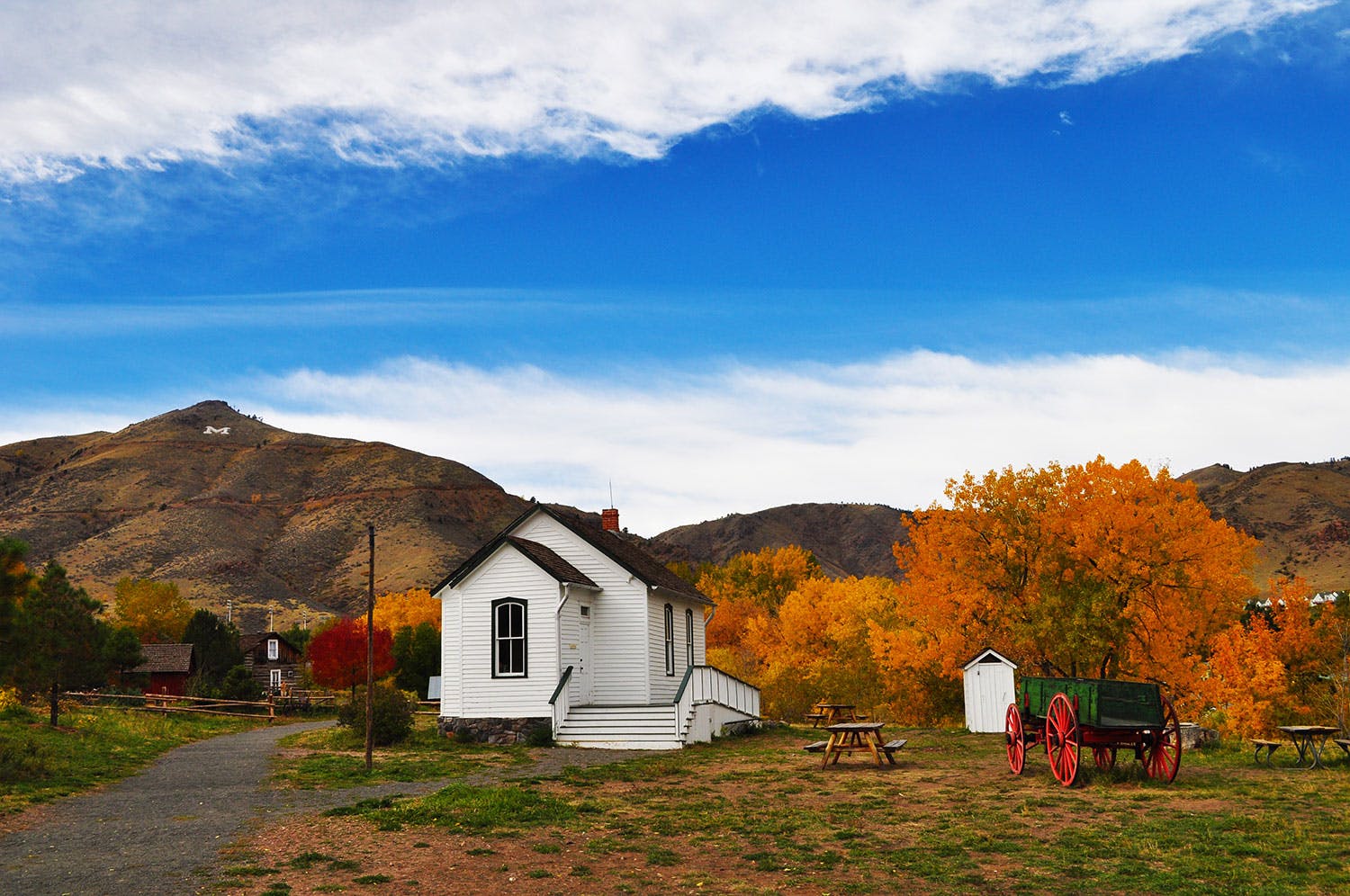 A dark-green wagon and small white building sit amid trees with orange leaves in Golden, Colorado.