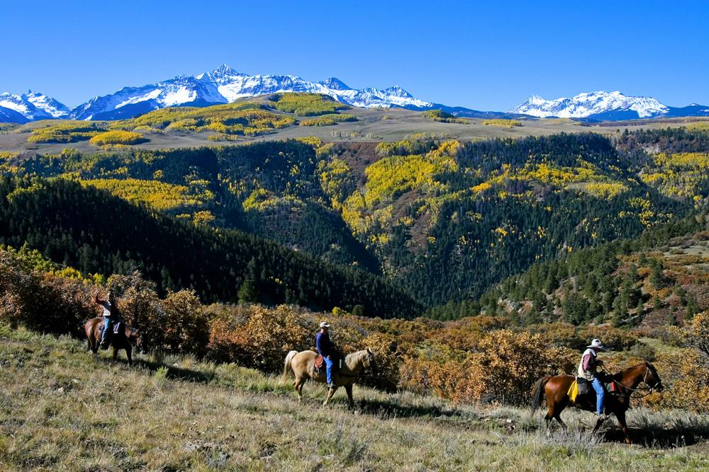 A group of riders travel mountainous lands near Telluride, Colorado. In the distance are snow-capped mountain peaks.