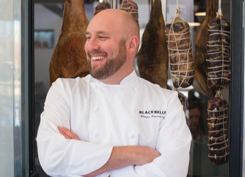 Top Chef Winner and Boulder chef Hosea Rosenberg smiles and crosses their arms as they pose for a photo in their white chef coat.