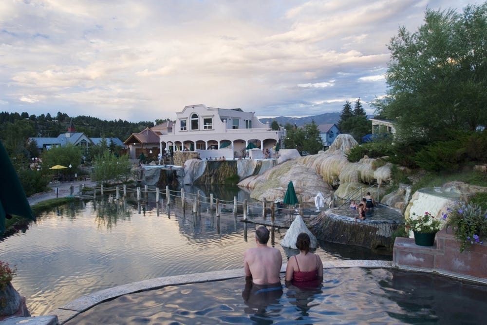 A couple soaks in a natural hot springs and looks out the pools below them at The Springs Resort & Spa in Pagosa Springs.