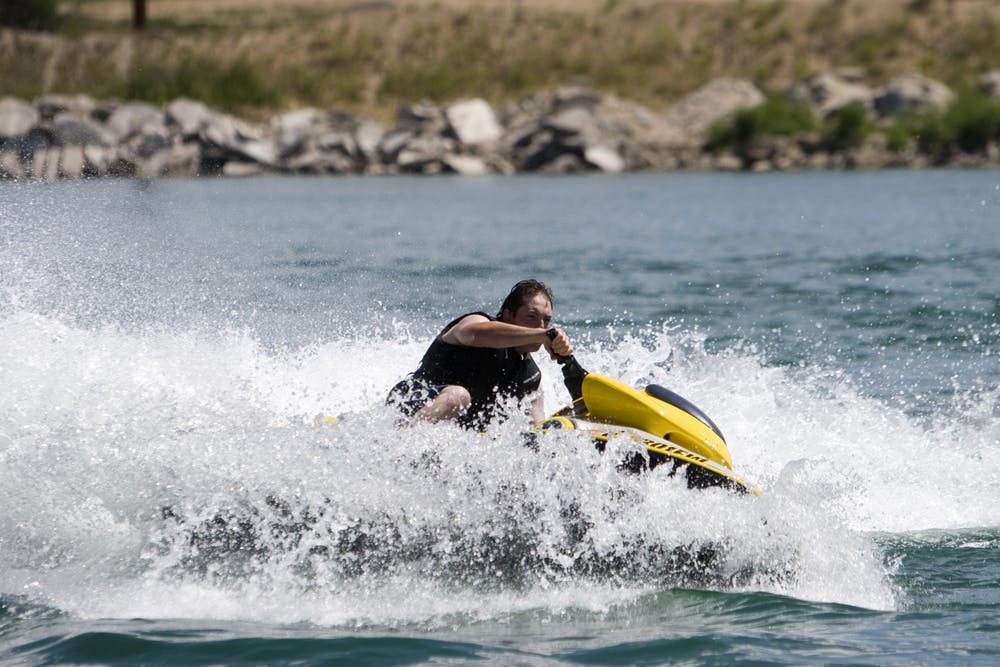 A man splashes through the waves on a yellow Jet Ski on a blue lake with a rocky shore