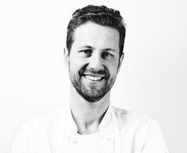 In a black and white shot, Lachlan Mackinnon-Patterson of Boulder's Frasca Food & Wine, smiles and looks directly into the camera.