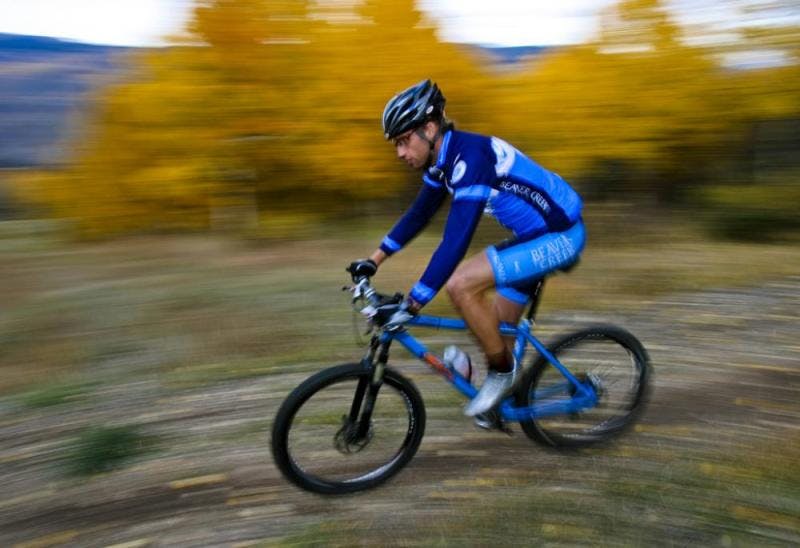 A rider decked out in a blue cycling outfit speeds down a golden-tree-lined trail near Avon, Colorado.