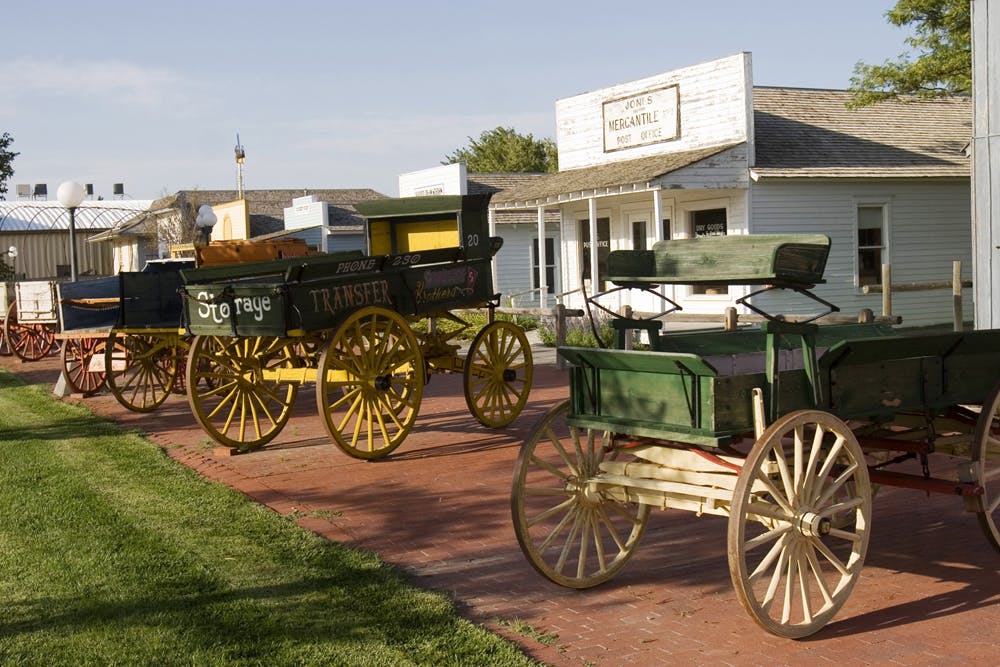 A row of painted wood wagons rest outside on a red-brick walkway at the Old Town Museum in Burlington.