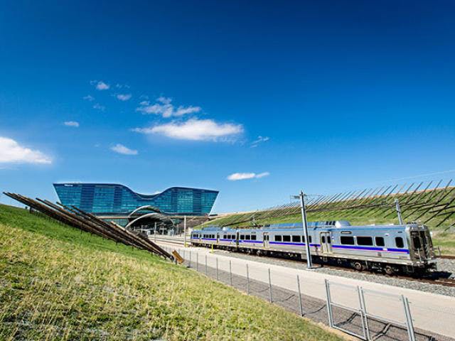 Denver's RTD train moves along the tracks on a sunny day surrounded by green grass