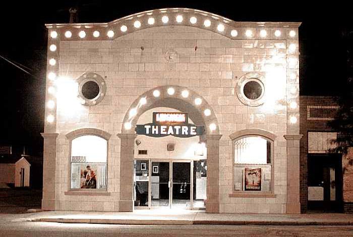 In Julesburg, Colorado, stands a small stone theater with marque-style lighting around the entrance and roof.