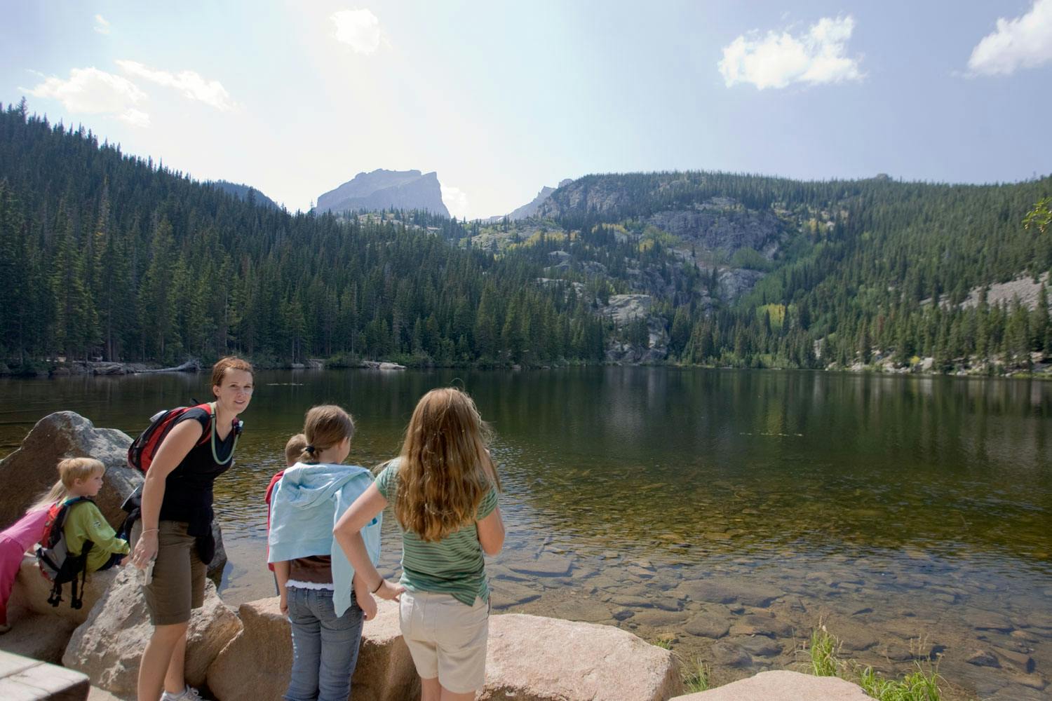 An adult and several children stand near the edge of Bear Lake along a trail near Estes Park, Colorado.