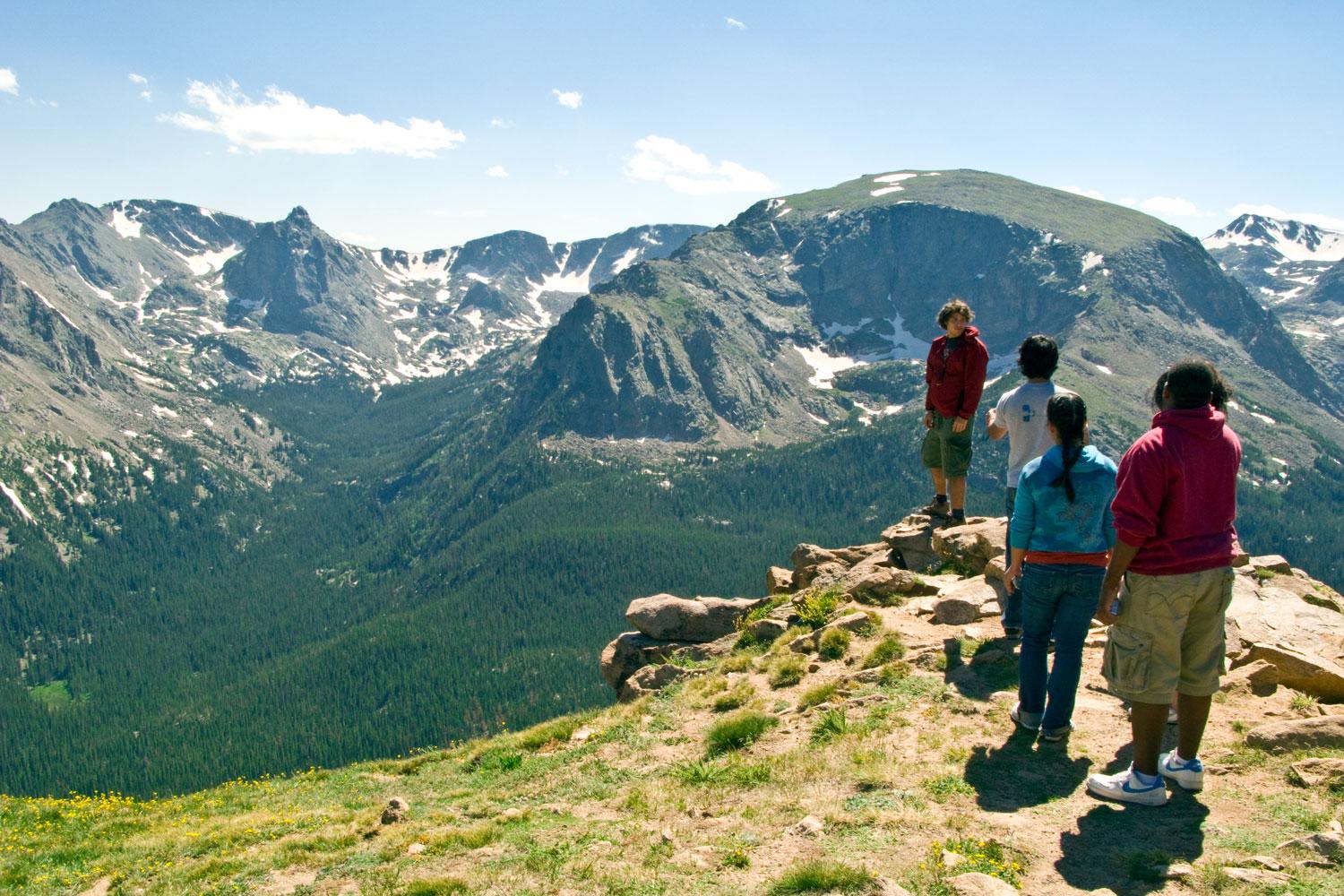 A group of hikers stop at a rocky outcropping to admire the view of the forested valley below in Rocky Mountain National Park.