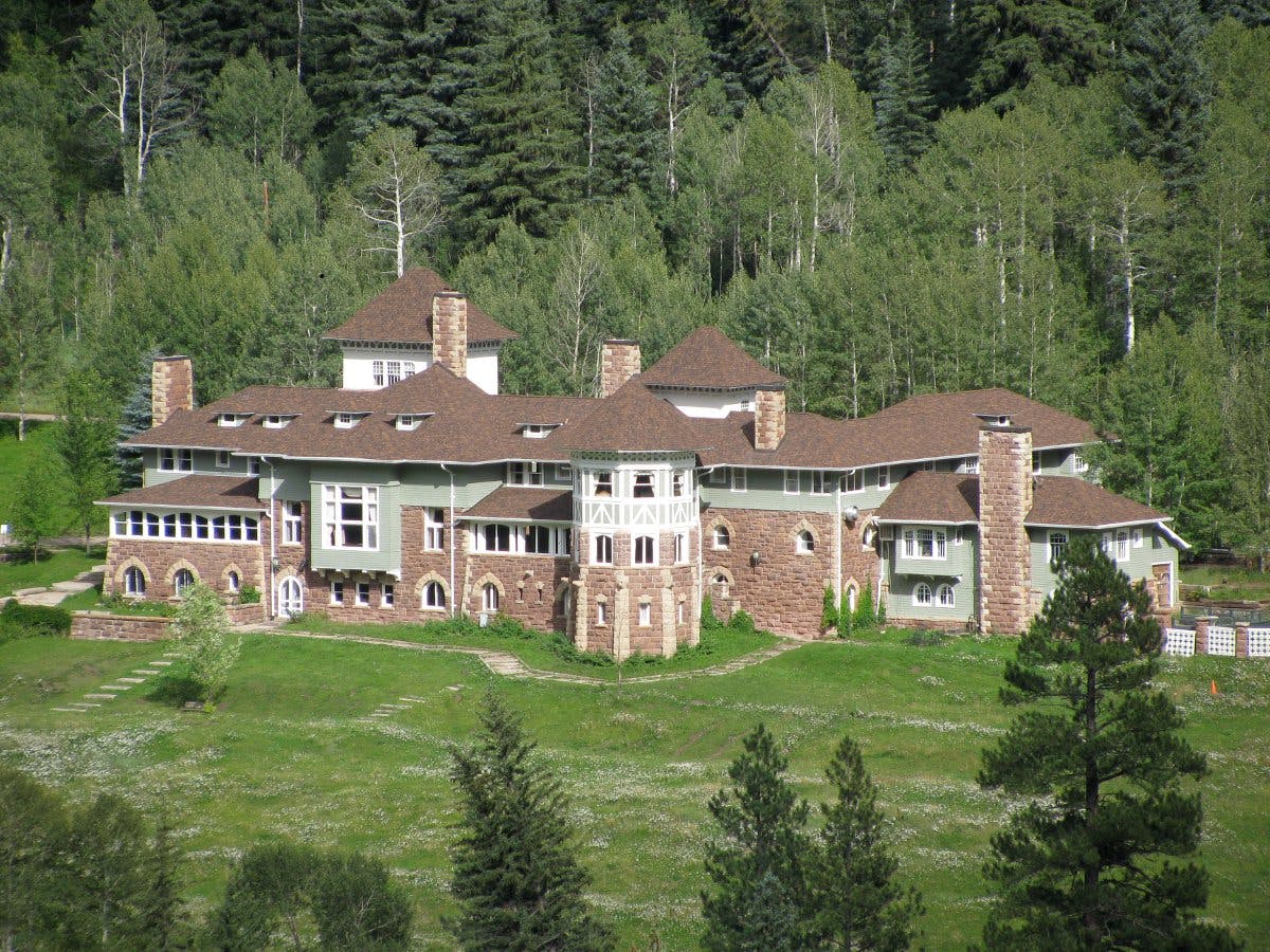 The Redstone Castle sits in a green field of grass surrounded by green-leafed aspens.