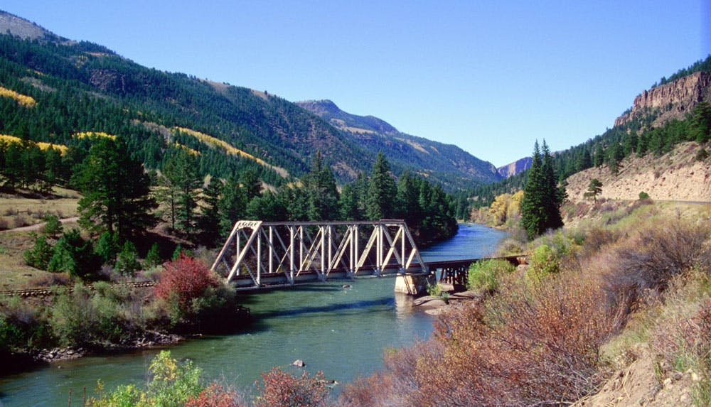 A train bridge spans the gently flowing Rio Grande