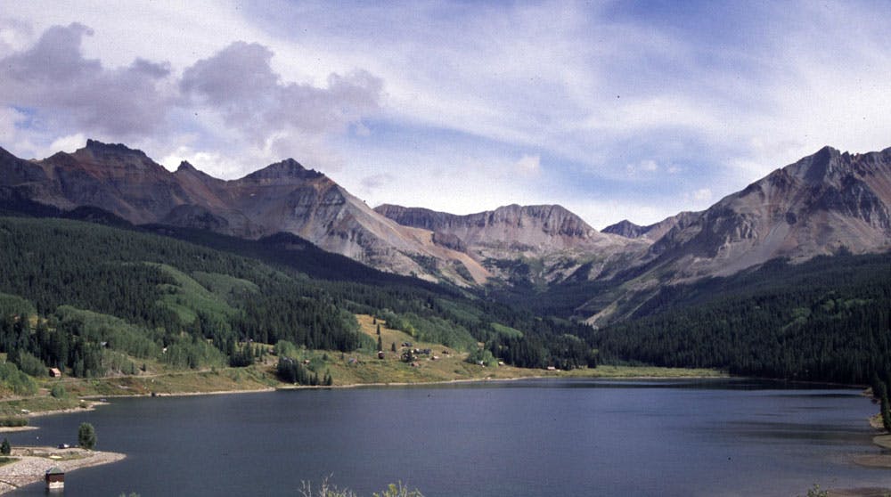 A mountain ridge, partly illuminated by the sun, wraps around a blue lake