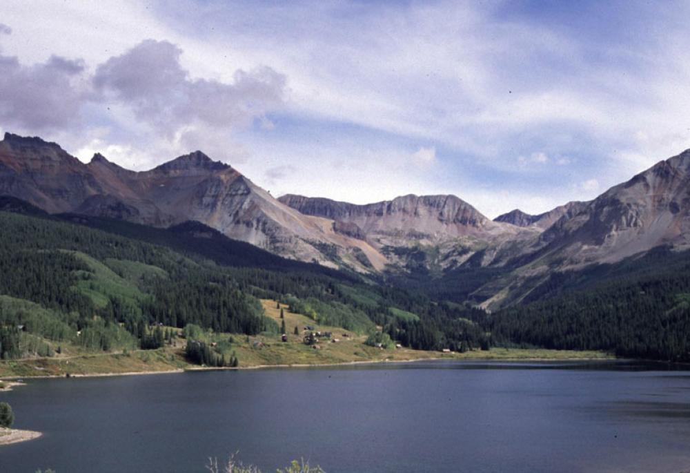 A mountain ridge, partly illuminated by the sun, wraps around a blue lake