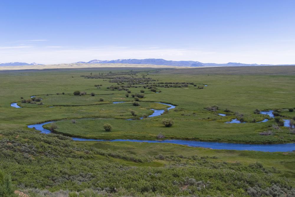 A river winds through a grassy valley with mountains in the distance