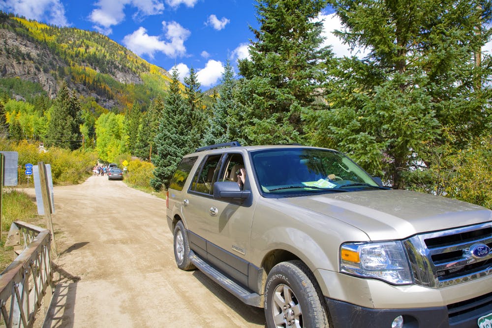 A car drives across a small bridge with mountains and blue sky in the background