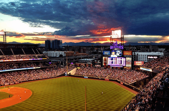 The sun sets behind a baseball field lit up at night