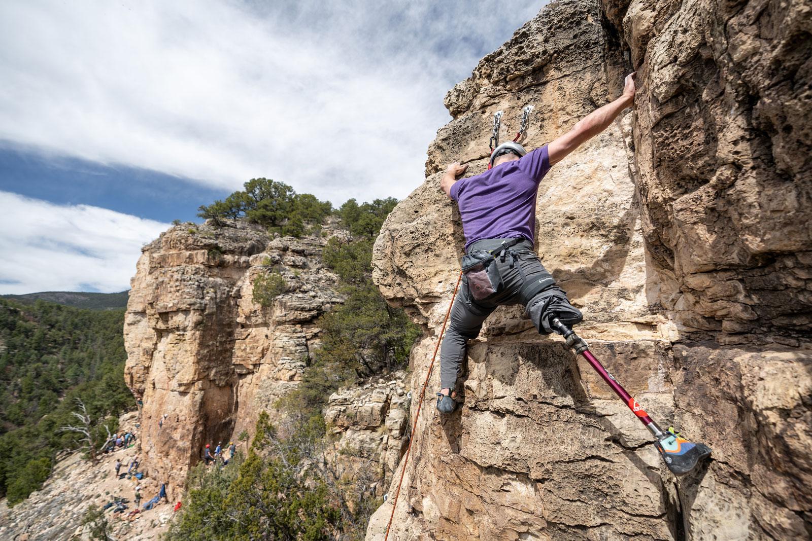 A climber in a purple shirt with an adaptive climbing leg scales around a rock face in Colorado.