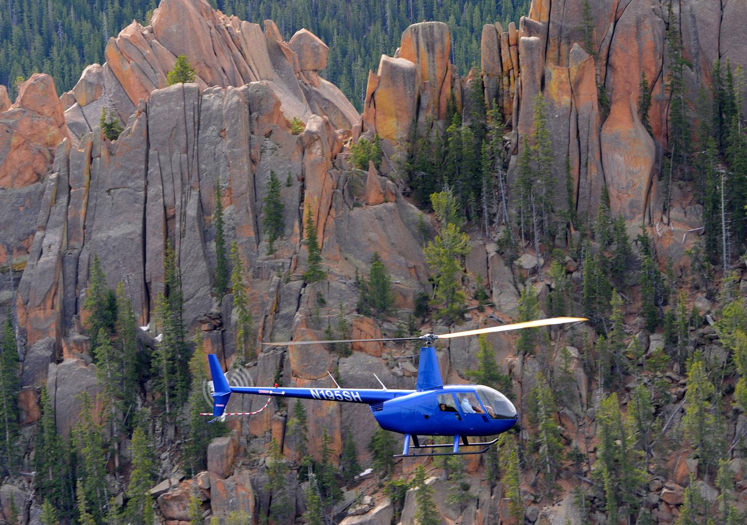 A helicopter tour flies past rocky mountain peaks