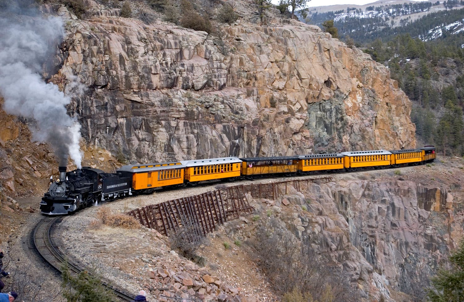 A train rolls past a rocky mountain pass