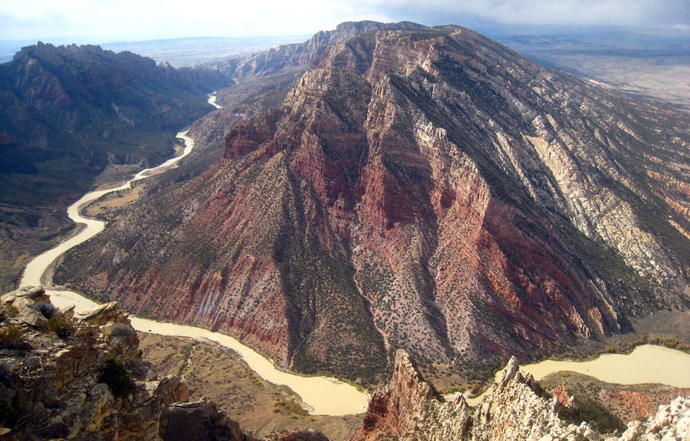 The twisting waters of the Yampa River weave around the base of a red and white rock mountain peak that's dotted green trees near Dinosaur National Monument in Colorado.