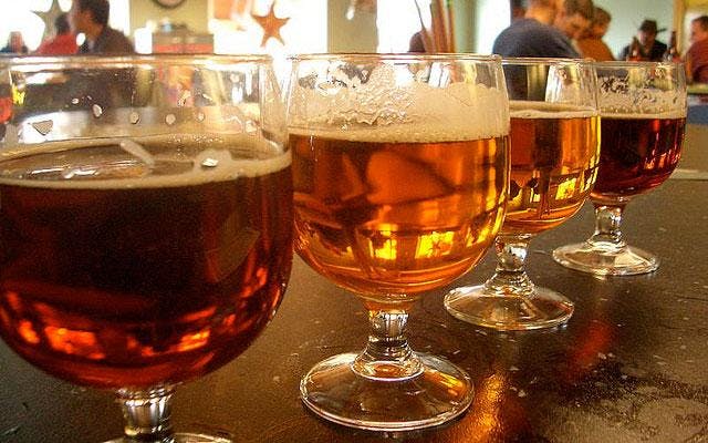 Four stemmed beer glasses stand side by side on a bar counter in Colorado. Each holds a rich, amber-colored beer with a rim of froth.