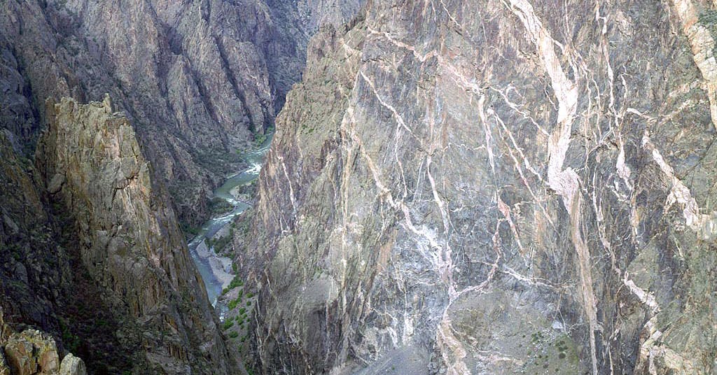 A zip zagging river flows swiftly at the bottom of the steep, white-streaked gray canyon walls of Black Canyon of the Gunnison National Park near Montrose, Colorado.