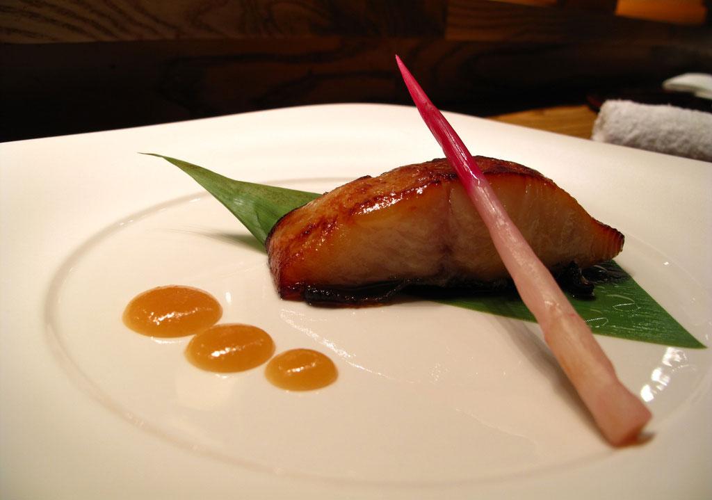 A slab of broiled black cod is artfully plated on a leaf with a single vegetable spear and three drops of sauce at Matsuhisa in Aspen, Colorado.