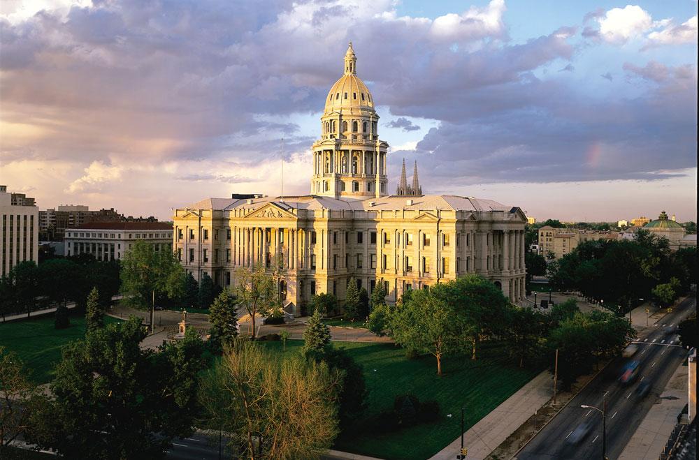 The white marbled Colorado Capitol building surrounded by green trees