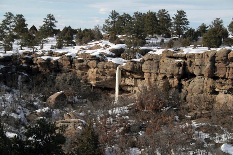 Water frozen in midair drops from the top of a rocky ridge into the canyon below. 