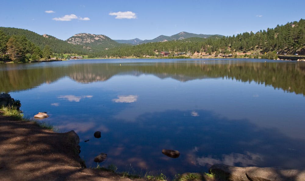 And evergreen-forested shoreline and a few clouds are reflected in a still lake