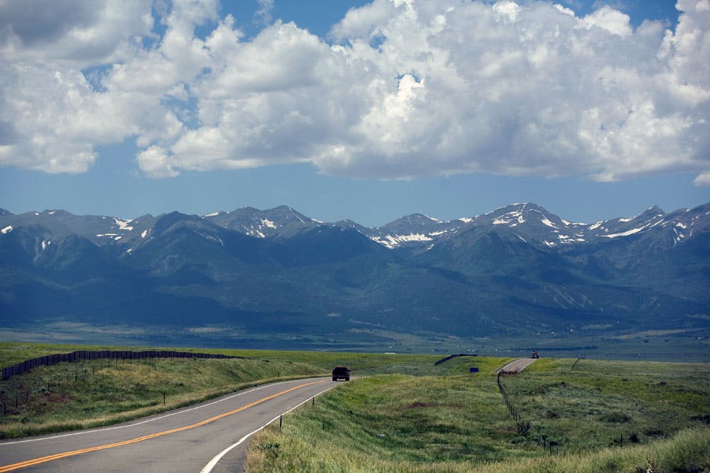 A car drives down a long stretch of road with towering mountains in the distance